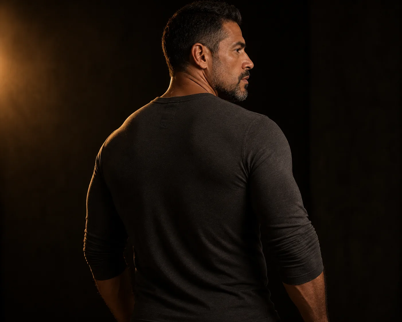 Back view of a man in a fitted dark shirt in a warm, low-lit room