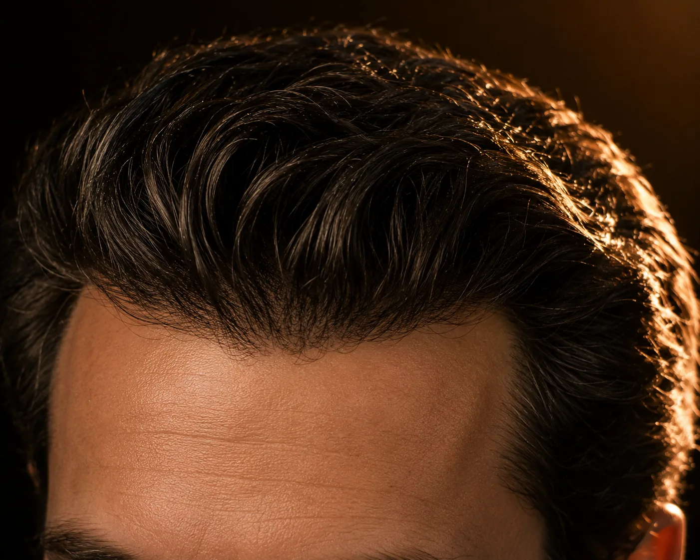 Close view of thick, swept-back hair at a man's crown in warm light